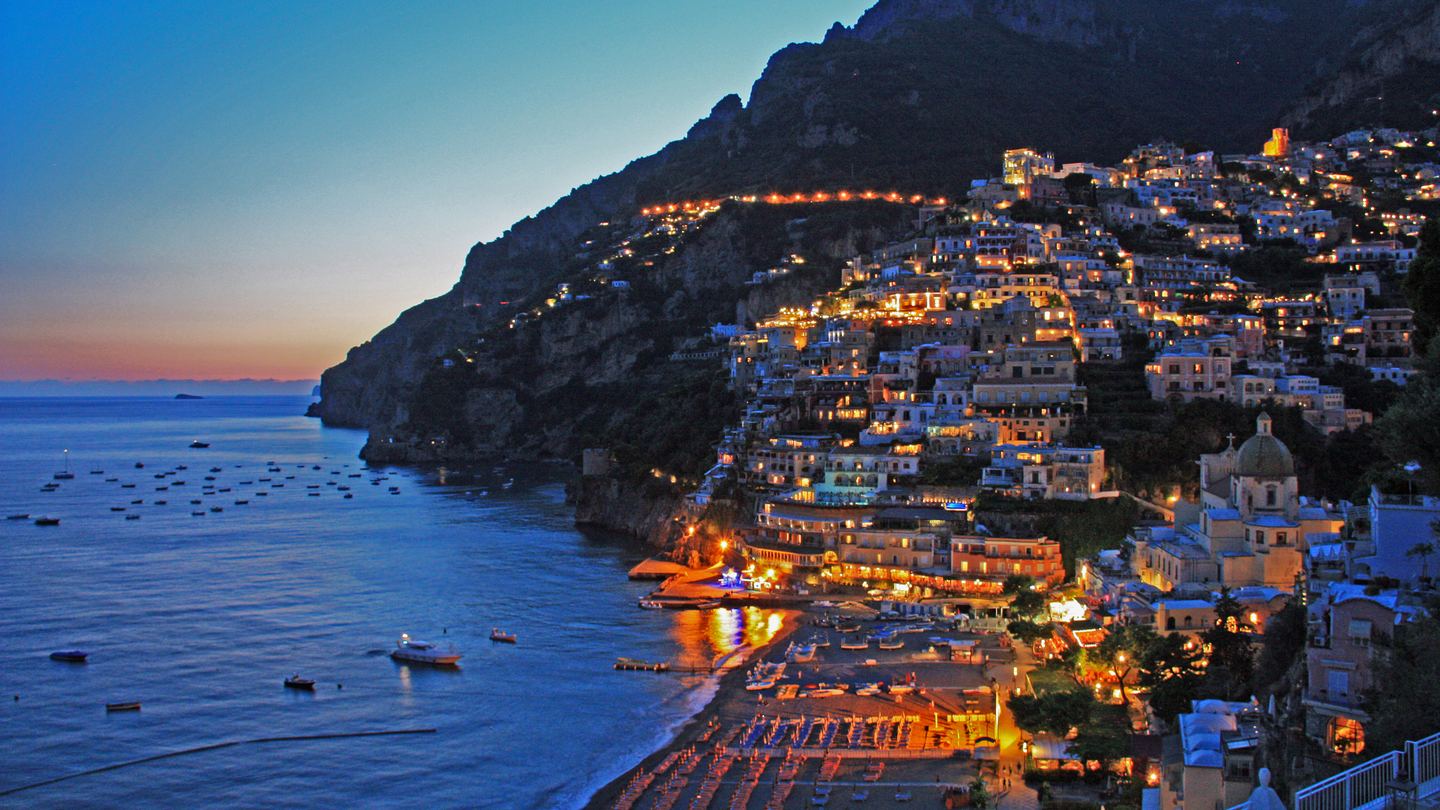 Warm lights along Positano's hillside above the blue sea at twilight
