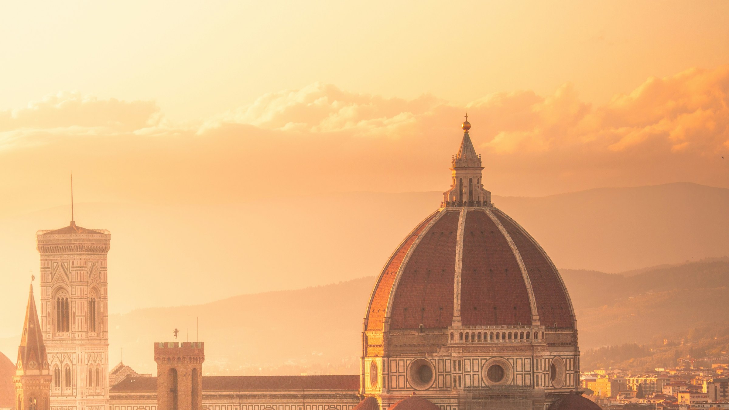 Florence Cathedral and Giotto's bell tower above terracotta rooftops in golden sunset light