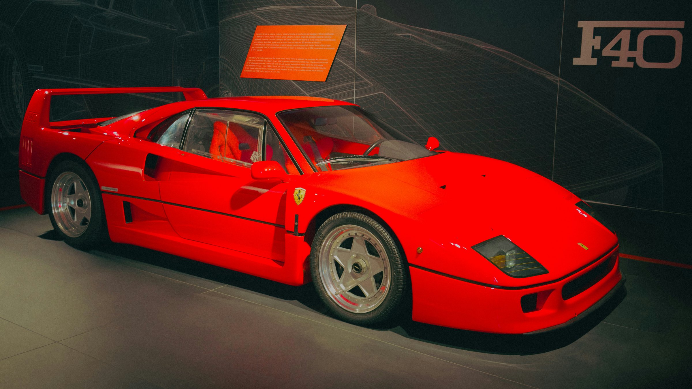 A red Ferrari F40 under dramatic warm light in the Maranello museum display