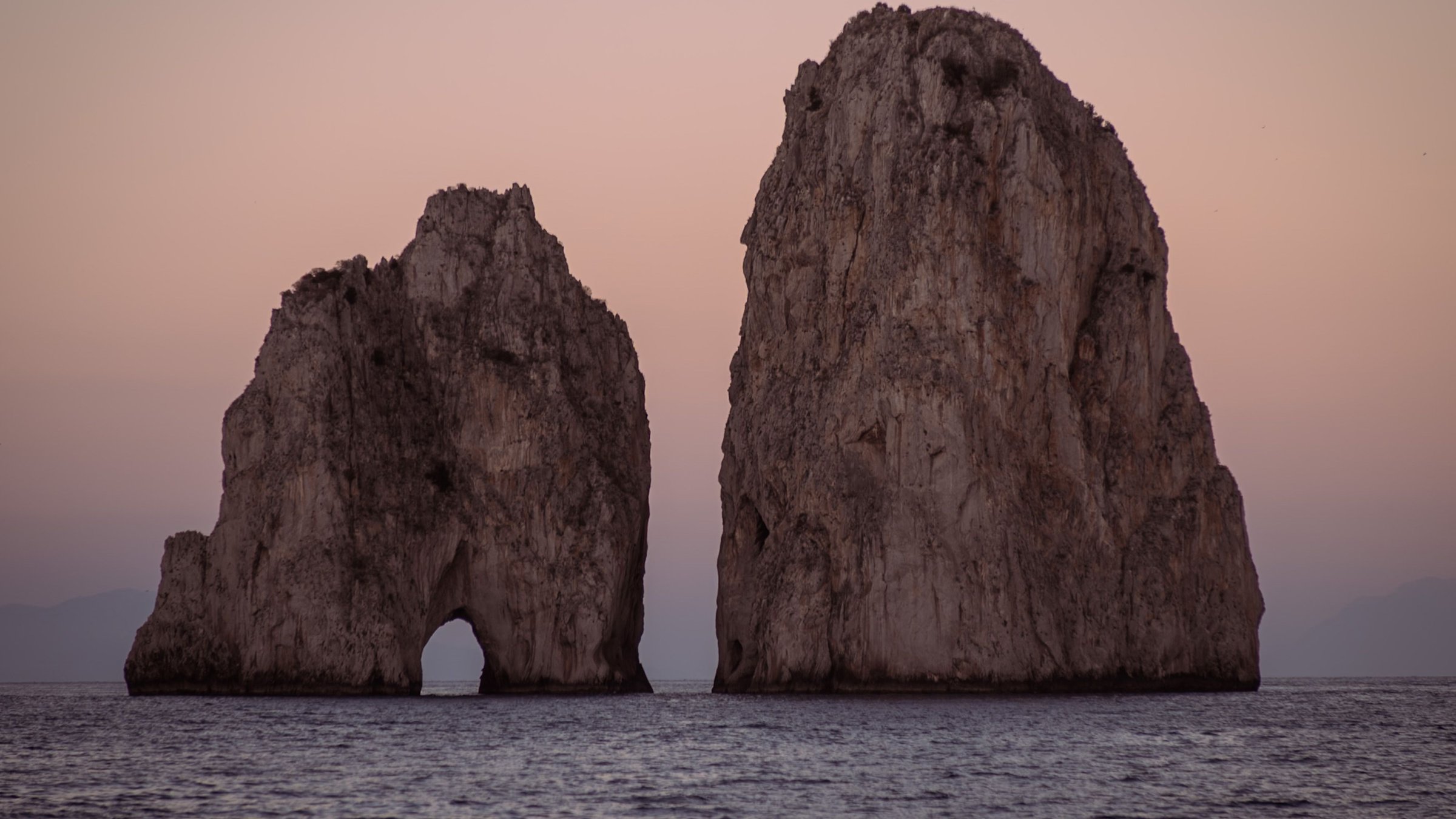Capri's Faraglioni rising from the sea against a soft pink sky