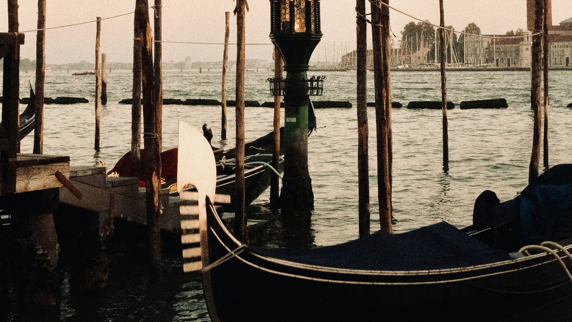 Dark gondolas and wooden mooring poles in warm evening light, with San Giorgio Maggiore across the Venetian water