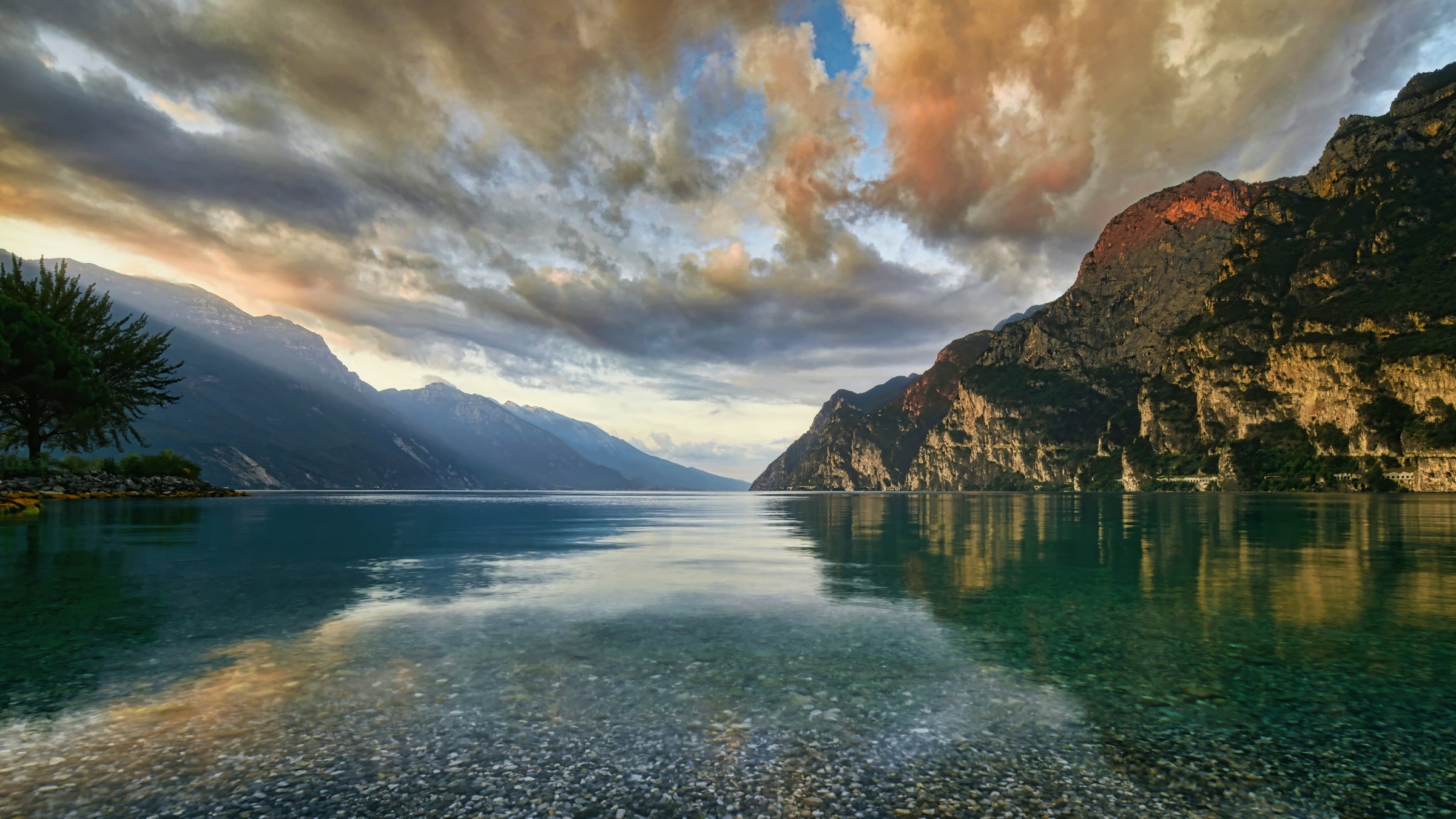Golden light and dramatic clouds above Lake Garda, with mountains reflected in clear, still water