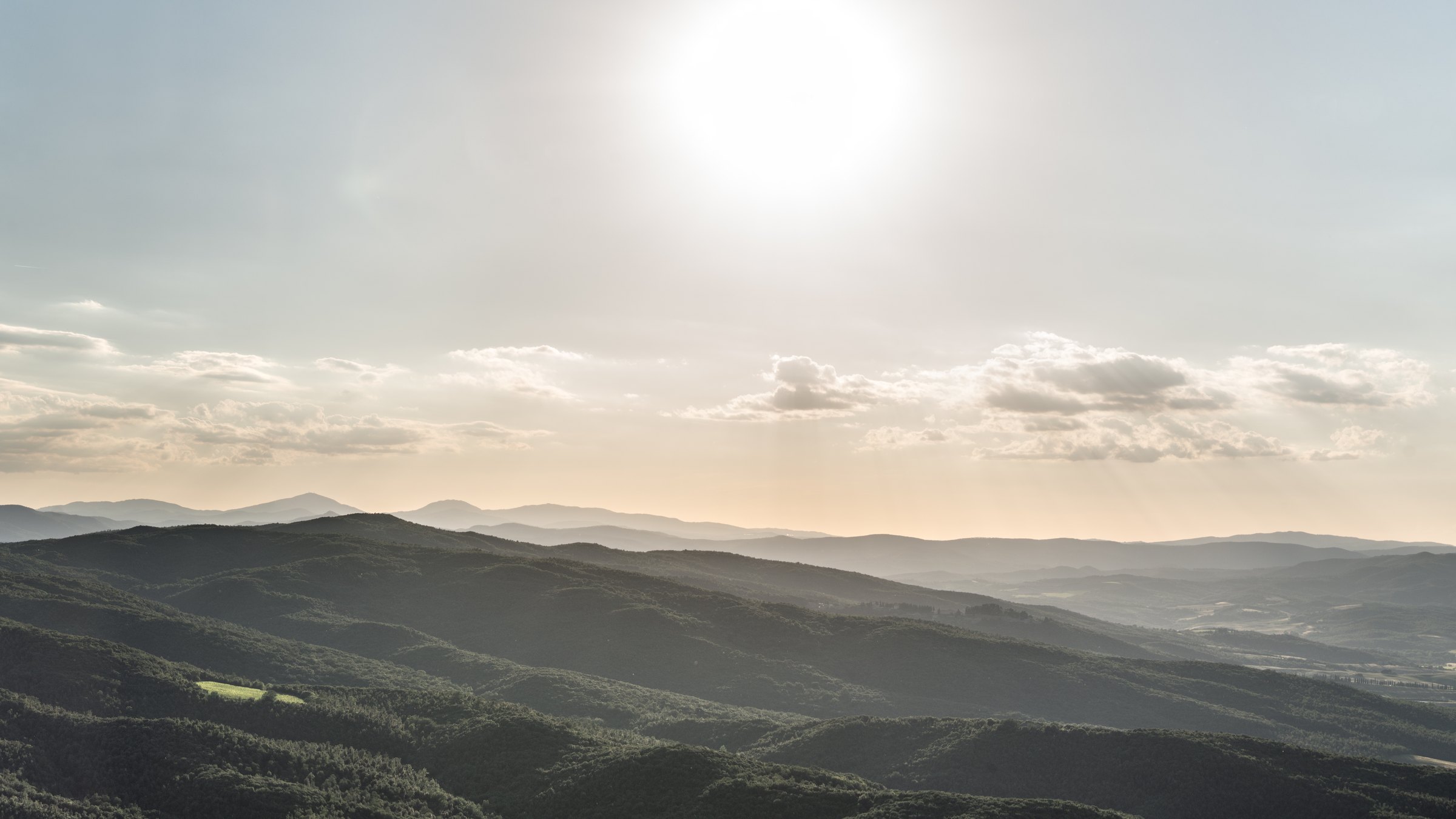 Layered hills near Montalcino in low golden light beneath a pale blue sky and bright sun