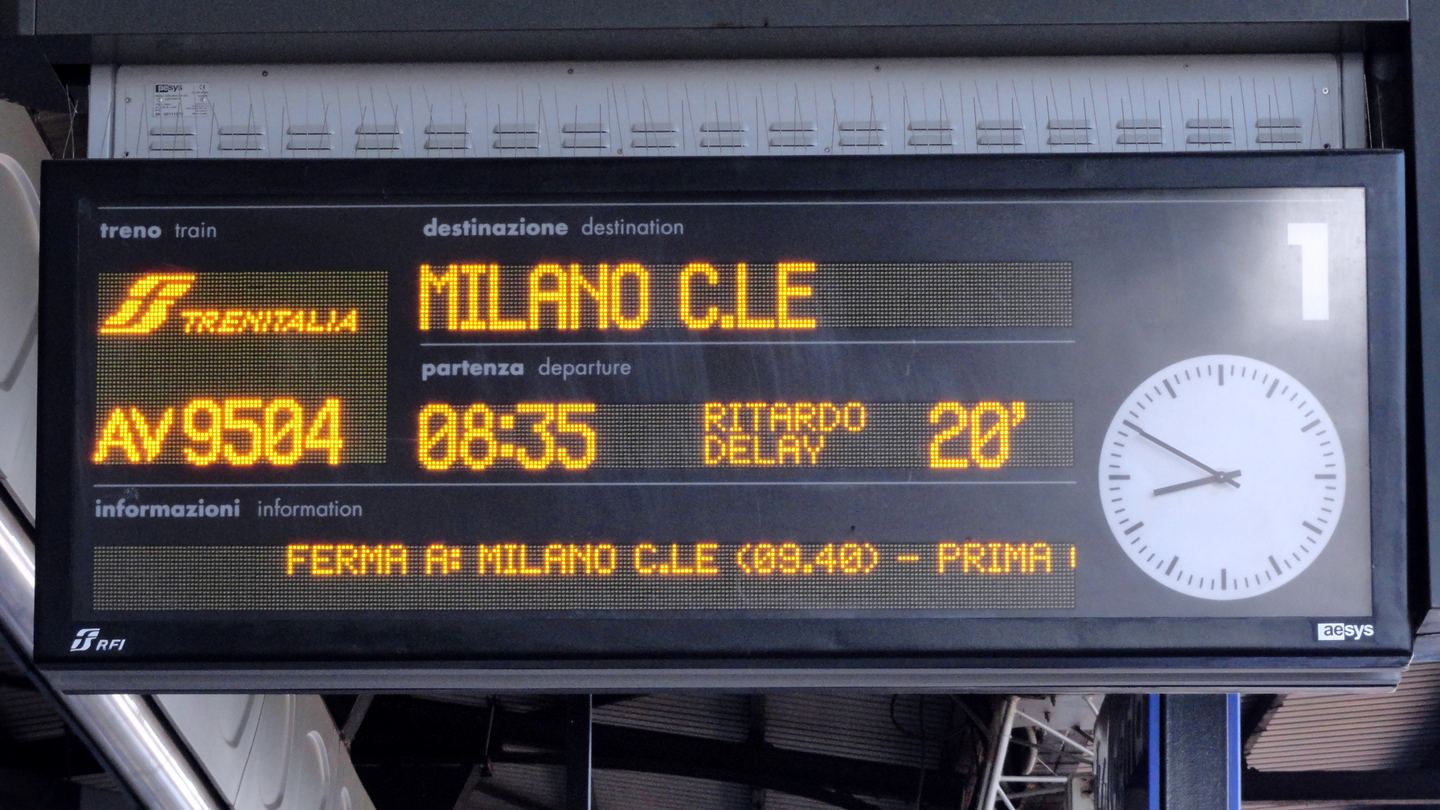 Electronic departure board at Bologna Centrale showing a Milan train delayed twenty minutes