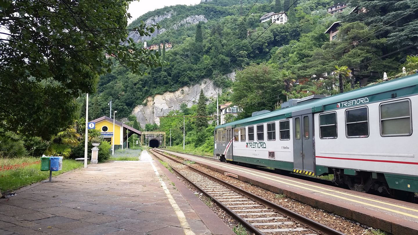 A regional train at Varenna station, with hillside houses and trees beyond the platform